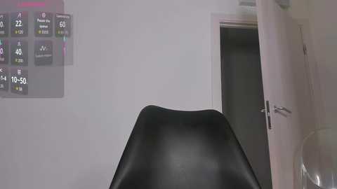 Video of a minimalist room with a black leather chair in the foreground, a white door slightly ajar, and a wall-mounted digital clock displaying 15:39. The room has a clean, modern aesthetic.