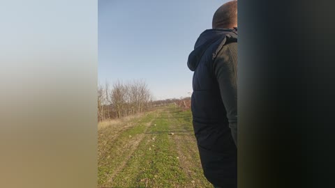 Video of a man in a dark jacket standing on a foggy rural path with sparse vegetation and leafless trees under a clear sky.