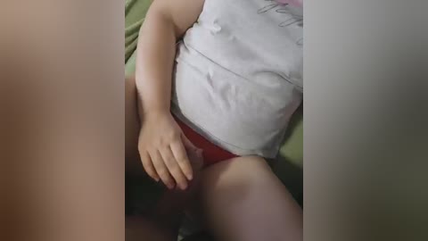 Video of a person lying on a green bedspread, wearing a white tank top and red panties. The person's left hand is resting on their thigh, partially obscuring the view.