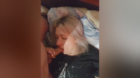 Video of a blonde woman with fair skin performing oral sex on a naked man's erect penis, lying on a bed with a floral-patterned pillow.