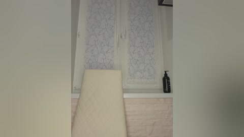 A video of a minimalist bathroom with a beige towel draped over a white sink, light wood vanity, and white-framed frosted glass shower door with floral pattern.