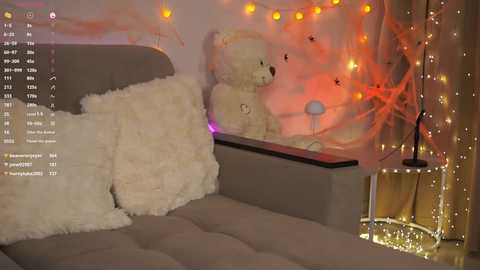 A cozy, dimly lit room with a plush white bear and pillow on a gray sofa, adorned with warm string lights and a small lamp.