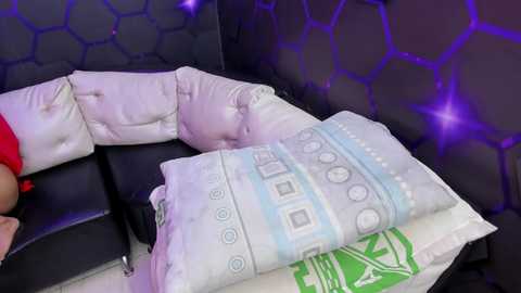 A video of a plush, cushioned black leather chair with a hexagonal-patterned purple backrest, featuring a person lying on it, partially covered by light blue and white patterned blankets.