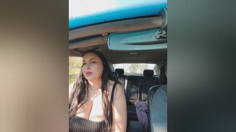 Video of a Latina woman with long black hair and fair skin, wearing a low-cut black top, sitting in a car with a blue sunroof.