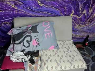 Video of a bed with a beige headboard, featuring a gray pillow with a black cat design, and a pink pillow with \"LOVE\" in bold letters. Purple, swirling-patterned wall in the background.