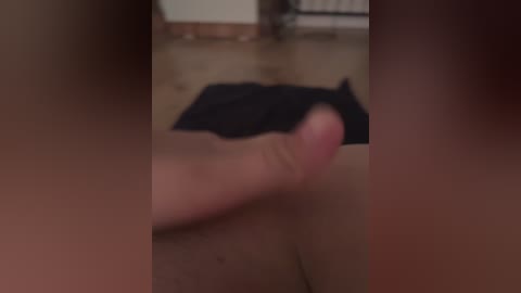 Blurry video of a hand holding a flaccid penis, partially visible in a dimly lit room with wooden flooring and a bed in the background.