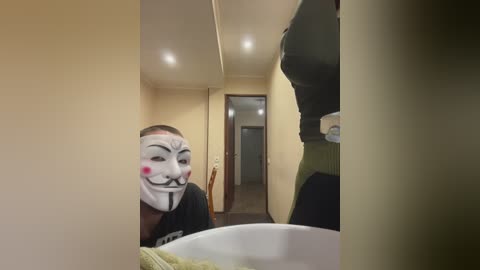 Video of a person in a dark room wearing a white mask with black and red details, looking into a mirror.