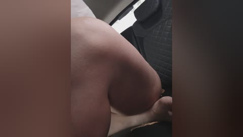 A close-up video of a person's bare buttocks and backside in a car, with a dark leather seat and light interior visible.