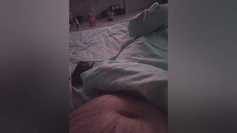 Video of a dimly lit bedroom with a person's leg under a green and white striped bedsheet, a digital clock on a bedside table, and a soft, muted color palette.