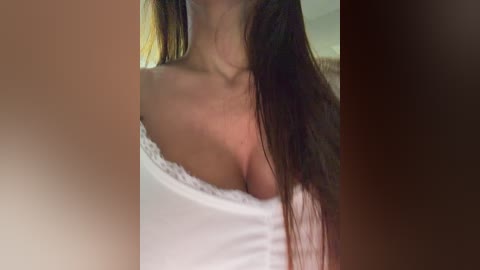 A close-up video of a woman with long brown hair, wearing a white, off-the-shoulder top, revealing cleavage. The background is blurred, suggesting an indoor setting with soft lighting.