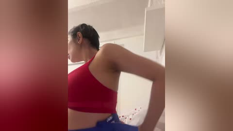 Video of a fit woman with medium skin tone, dark hair, and athletic build, wearing a red sports bra and blue pants, bending over, with a messy, bloodied floor in the background.