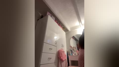 Video of a girl in a bathroom, with a white cabinet, pink towel, and a mirror; the room is dimly lit.