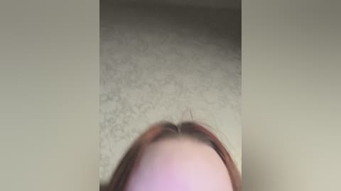 Video of a person from a low angle, focusing on their head with light brown hair. The background shows a beige carpeted floor. The image is slightly blurred, possibly due to motion.