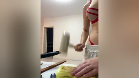 Video of a woman in a red bikini with white straps, chopping vegetables on a counter in a brightly lit kitchen.