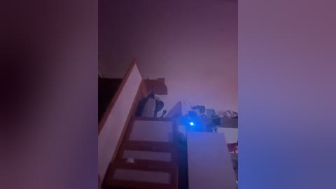 A dimly-lit video of a narrow staircase leading to a cluttered kitchen area, with a bright blue light source casting a glow in the background.