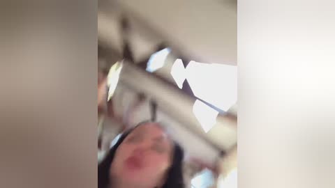 A blurred video of a person with fair skin and dark hair, captured from an overhead angle, displaying a white ceiling with geometric patterns and soft lighting.