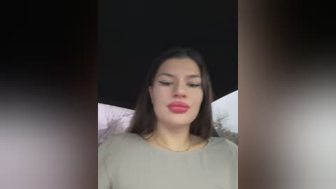 Video of a woman with long dark hair and fair skin, wearing a beige blouse, against a blurred, dark background.