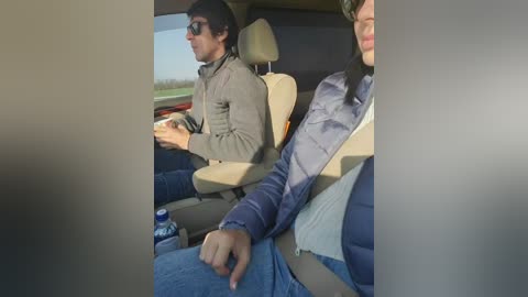 Video of two men in a car: one wearing a gray jacket and sunglasses, the other in a blue jacket and puffy vest, both drinking from cans.