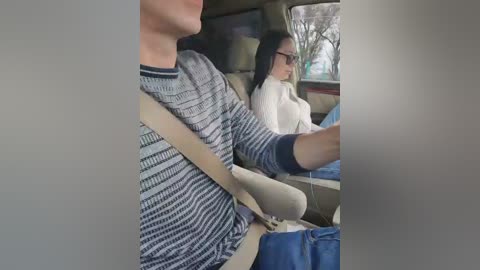 Video of a man in a striped sweater driving a car, with a woman in a white sweater and sunglasses in the passenger seat, both looking forward.