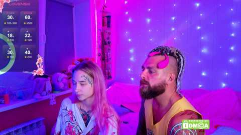 Video of two people in a dimly lit room, purple lights and fairy lights in the background, watching a video game on a TV screen.