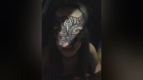 Video of a woman with long black hair, wearing a black lace mask, with a dark, shadowy background, evoking a mysterious, gothic atmosphere.