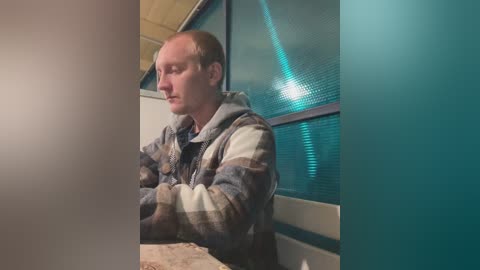 Video of a bald, middle-aged white man in a striped sweater, sitting with arms crossed, against a teal, glass-walled room with wooden ceiling.