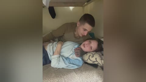 A video shows a man leaning over a woman lying on a beige carpet in a small, dimly lit room. The woman wears a blue sweater, and the man is in a brown shirt.