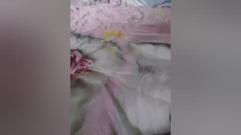 A video shows a close-up of a bed with a tangled, pastel-colored comforter, featuring pink, green, and white hues. The image is slightly blurred, making it difficult to discern details.