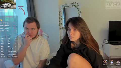 Video of a young man and woman in casual clothes, looking serious, in a bedroom with a computer screen showing a car.