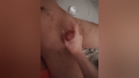 Video of a close-up of a person's hand squeezing a small, dark nipple. The background features a light-colored, textured surface, possibly a wall or fabric.