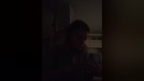 Video of a dimly lit room with a man in silhouette, partially obscured by a doorway, holding a phone to his ear. The background shows a shelf with a few items.