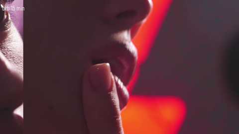 A close-up video of a woman's lips and nose, with a red neon sign in the background. She has a light skin tone, and her lips are slightly parted. The image is intimate and sensual.