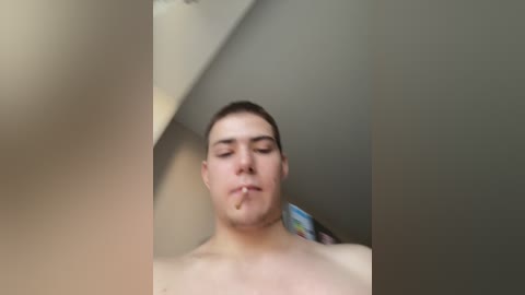Video of a young, fair-skinned, shirtless man with short brown hair, smoking a cigarette, set against a plain beige wall.
