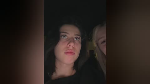 Video of a young woman with dark hair and fair skin, wearing a black top, looking confused and slightly upset. She's partially hidden by another person's arm.