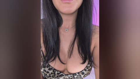 Video of a woman with long, straight black hair, wearing a leopard-print bra, showing cleavage, and a heart necklace. Background is blurred.