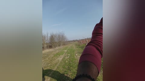 Video of a person wearing a maroon sweater and socks, standing on a dirt path with a clear blue sky and sparse trees in the background.