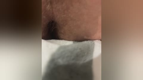 Video of a close-up view of a person's inner thigh and pubic area, showing light brown skin, sparse hair, and a towel partially covering the groin. The background is blurred and neutral-toned.