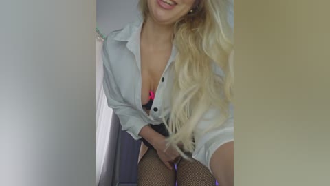 A video of a smiling, blonde woman with fair skin, wearing an unbuttoned white shirt revealing a pink bra, black skirt, and fishnet stockings. She stands in a dimly lit hallway.