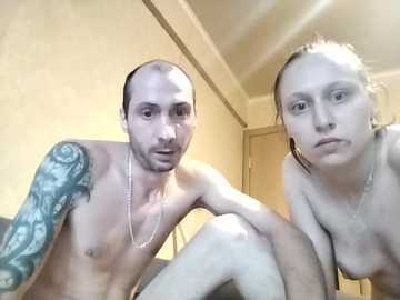 Video of a topless man with a large tattooed arm and a topless woman with light skin and dark hair, both indoors.