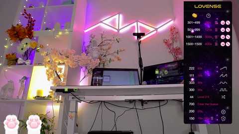 Video of a modern, brightly lit room with white shelves adorned with flowers, a white desk with a laptop and monitor, and a pink neon sign.