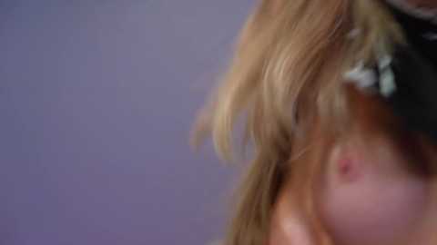A close-up video of a blonde woman with a pale complexion, medium-sized breasts, and a black headband, blurred background.