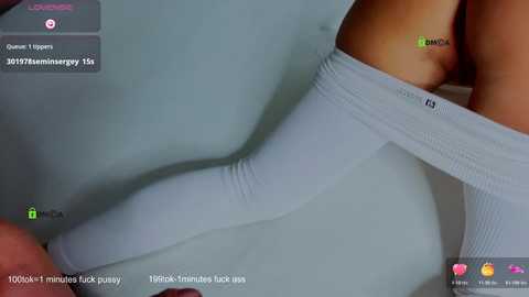 A close-up video of a woman's leg in a white, ribbed, knee-high sock, with her thigh exposed, captured on a mobile phone screen. The image is grainy, possibly taken in a dimly lit room.