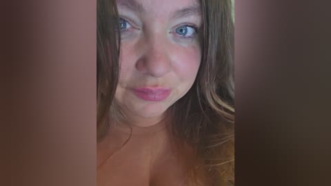 Video of a Caucasian woman with long, light brown hair, blue eyes, and light skin, making a pouty face. Her bare shoulders are visible, indicating a topless state.