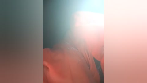 A blurry video featuring a person's head, likely male, with visible facial features and a slightly raised eyebrow, surrounded by a soft, pinkish glow.