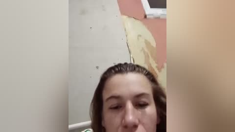 Video of a young woman with wet hair, partially covered by a yellow plastic tarp, in a room with beige walls and a white ceiling, suggesting a construction site or renovation.