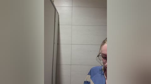 A video of a person with glasses and a blue shirt, partially obscured by beige walls and tiles, creating a sense of mystery.