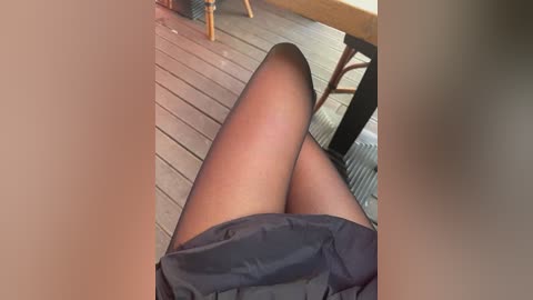 A video of a woman's legs in black stockings, reclining on a wooden deck with a chair and table in the background.