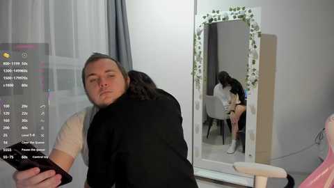 Video of a man with short gray hair, wearing a white T-shirt and black jacket, sitting on a pink chair. He's asleep with his head on a woman's shoulder, who is seated at a table in the background.