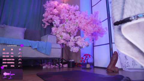 Video of a dimly lit, modern bedroom with a large cherry blossom tree, blue curtains, and a white futon.