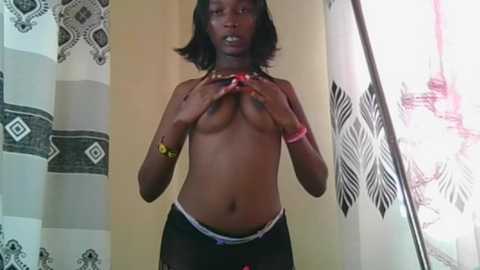 A video of a topless, slender African woman with medium-sized breasts, dark skin, and shoulder-length black hair, wearing black panties and a yellow wristband. She stands in a bathroom with patterned shower curtains.